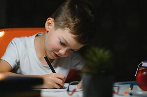 jongen aan het doen huiswerk Bij huis in avond foto