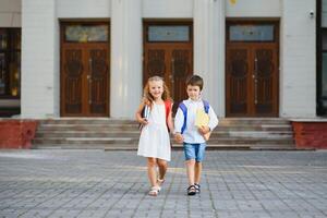 gelukkig kinderen Gaan terug naar school. leerling van primair school- Gaan studie met rugzak buitenshuis. kinderen Gaan hand- in hand. begin van lessen. eerste dag van val. jongen en meisje van elementair leerling. foto