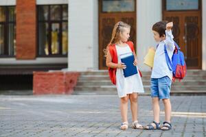 kinderen Gaan terug naar school. begin van nieuw school- jaar na zomer vakantie. jongen en meisje met rugzak en boeken Aan eerste school- dag. foto