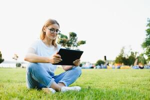 vrouw college leerling gebruik tablet pc zitten Aan gras foto
