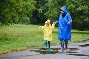 mam en zoon in regenjassen hebben pret samen in de regen. concept van familie vakantie en gelukkig jeugd. foto