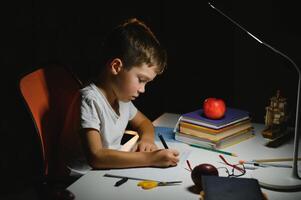 jongen leren lessen in de huis instelling Bij de tafel in de licht van een tafel lamp. foto