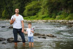 een vader onderwijs zijn zoon hoe naar vis Aan een rivier- buiten in zomer zonneschijn. vader dag. foto