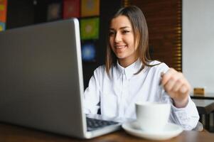 portret van een jong vrouw freelancer gebruik makend van laptop computer voor afstand baan terwijl zittend in modern koffie winkel interieur, slim blond vrouw werken Aan netboek gedurende ochtend- ontbijt in cafe bar foto