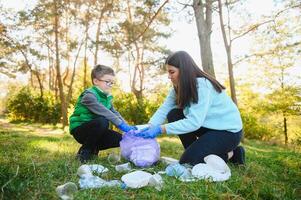 mam geeft les haar zoon naar schoon omhoog uitschot in natuur. een vrouw verwijdert plastic flessen in een tas. de onderwerp van milieu verontreiniging door afval. foto