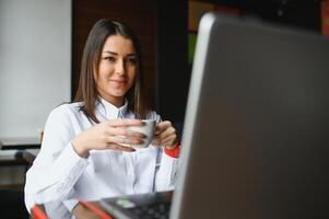 portret van een jong vrouw freelancer gebruik makend van laptop computer voor afstand baan terwijl zittend in modern koffie winkel interieur, slim blond vrouw werken Aan netboek gedurende ochtend- ontbijt in cafe bar foto