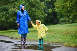 mam en zoon in regenjassen hebben pret samen in de regen. concept van familie vakantie en gelukkig jeugd. foto