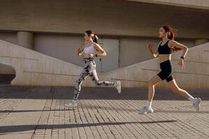 twee actief Dames atleet rennen Aan zonnig ochtend- kant door kant Aan modern gebouwen achtergrond foto