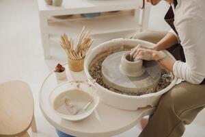 vrouw pottenbakker in schort maken vorm van klei vaas Aan spinnen pottenbakkerij gereedschap in keramisch werkplaats foto