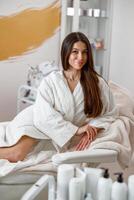 vrouw in wit badjas glimlachen Bij camera Aan ligbed in spa centrum foto
