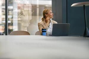 elegant bedrijf vrouw werken Aan laptop zittend de bureau Aan kantoor achtergrond en looks weg foto