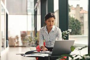 vrouw ondernemer werken Aan laptop terwijl zittend de bureau in modern samenwerken. hoog kwaliteit foto