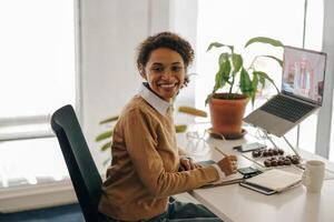 vrouw freelancer hebben video conferentie met cliënt en maken aantekeningen zittend in knus coworking foto