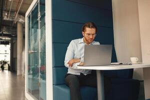 gefocust freelancer drinken koffie gedurende werken Aan laptop in modern coworking foto