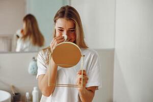 jong vrouw Verwijderen bedenken met katoen stootkussen in voorkant van spiegel staand in badkamer foto