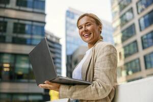 mooi volwassen vrouw manager werken laptop Aan modern gebouw achtergrond en looks camera foto