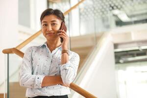 vrouw freelancer pratend telefoon terwijl staand in coworking Aan trap en op zoek Aan camera foto