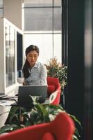 vrouw ondernemer werken Aan laptop en drinken koffie terwijl zittend de bureau in modern coworking foto
