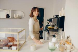 vrouw barista in schort gieten heet melk schuim in koffie. professioneel koffie brouwen concept foto