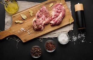 twee rauw varkensvlees nek steaks Aan een bord en specerijen voor Koken. top visie van zwart tafel. foto
