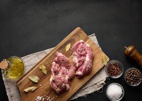 twee rauw varkensvlees nek steaks Aan een bord en specerijen voor Koken. top visie van zwart tafel foto