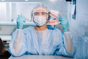 een tandheelkundig dokter vervelend blauw handschoenen en een masker houdt een tandheelkundig model- van de bovenste en lager kaken en een tandheelkundig spiegel foto