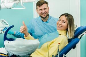 mooi meisje geduldig shows de klasse met haar hand- terwijl zittend in de tandarts stoel foto