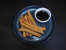 Mexicaans churros met saus geserveerd in een schotel geïsoleerd Aan donker achtergrond top visie foto