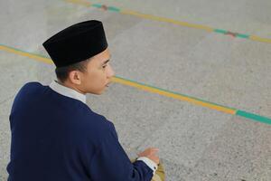 portret van religieus Aziatisch Mens in moslim overhemd bidden en aan het doen salat of sholat in moskee foto
