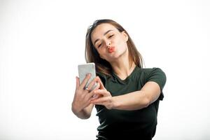 mooi meisje maakt haar lippen eend en nemen een zelf portret met haar slim telefoon. schattig lief jong vrouw maken eend gezicht en nemen selfie met mobiel telefoon over- wit achtergrond. foto