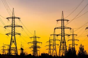 avond licht. zonsondergang gieten rood en oranje licht. silhouetten van de elektrisch macht masten en kabels, pylonen. elektriciteit macht station. foto