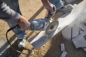 een Mens is gebruik makend van een Slijper naar besnoeiing een stuk van beton foto