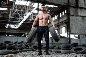 sterk jong Mens poseren Bij de verlaten plaats met banden Bij de achtergrond. groot spieren en perfect buikspieren. veel banden Aan de achtergrond. sterke man na training foto