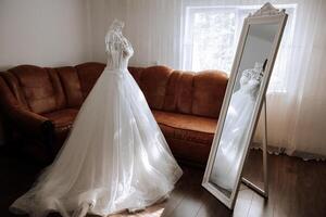 slaapkamer interieur met bruiloft jurk bereid voor de ceremonie. een mooi weelderig bruiloft jurk Aan een mannequin in een hotel kamer. foto