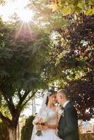 een jong bruid en bruidegom teder omhelzing in de stralen van de herfst zon. inschrijving en mooi jong meisje bruid. een Mens kusjes zijn geliefde. tegen de achtergrond van een mooi tuin foto
