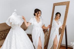 in de ochtend, een ongelooflijk mooi en luxueus bruid, gekleed in een wit gewaad, poses door de spiegel in haar slaapkamer. ochtend- van de bruid met een luxueus kapsel en natuurlijk verzinnen. foto