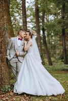 lief en elegant pasgetrouwden zijn knuffelen en glimlachen tegen de achtergrond van herfst natuur in een mooi tuin. een ongelooflijk mooi jong bruid leunde tegen de schouder van haar geliefde bruidegom foto