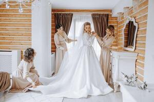 bruidsmeisjes verheugen in de ochtend, helpen naar vastmaken de toetsen Aan de bruiloft jurk en bereiden voor de bruiloft ceremonie. ze nemen afbeeldingen, glimlach, helpen de bruid met haar schoenen. foto