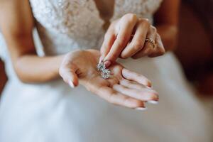 elegant bruid Holding zilver oorbellen. inschrijving handen met sieraden. jong bruid zet Aan haar bruiloft decoratie foto