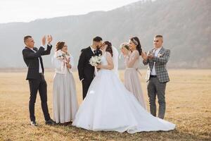 bruiloft foto sessie in natuur. de bruid en bruidegom kus en hun vrienden