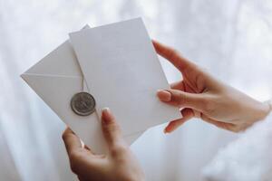 de bruid in haar handen houdt een wit envelop, een uitnodiging, een geschenk vel van papier. detailopname bruiloft fotografie, kopiëren ruimte, portret. foto