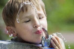 een kind drankjes water van een fontein. een Jet van water en een drinken Mens. dorst. foto
