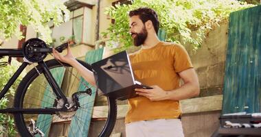 jong sportief Mens onderhouden en beveiligen wielersport uitrusting met de gebruik van internet en technologie. enthousiast sportief Kaukasisch mannetje met laptop repareren fiets in huis tuin. foto