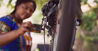 enthousiast Afrikaanse Amerikaans vrouw fietser voorzichtig onderzoeken en vaststelling beschadigd fiets. buitenshuis jong toegewijd zwart vrouw onderhouden prestatie van fiets componenten. in zoomen schot. foto