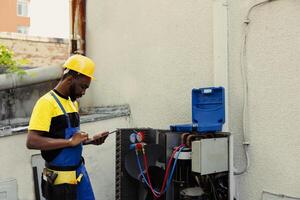 bekwaam monteur aan het doen lucht conditioner controle, op zoek voor lekken en andere vereist reparaties naar voorkomen majoor storingen. bedreven klusjesman probleemoplossen condensor, schrijven bevindingen Aan klembord foto