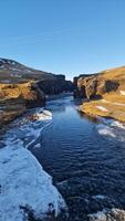 besneeuwd IJslands Ravijn met bevroren water stroom en kliffen gedekt in vorst creëren prachtig landschap visie. magisch fjadrargljufur Ravijn met rivier- stromen in IJsland tussen hellingen. foto