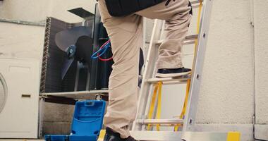 grond niveau schot van bekwaam elektricien Holding hand- boren beklimming vouwen ladder naar Doen onderhoud Aan op het dak hvac systeem. gekruid draadman in opdracht naar controle Aan condensor foto