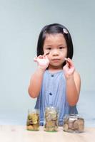 portret in beeld. Aziatisch kindmeisje dat zilveren muntstukken in haar handen houdt. geld sparen voor de toekomst. munten contant in graspot. op houten tafel. geïsoleerde schone achtergrond.
