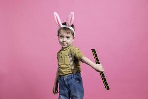 positief vrolijk kleuter spelen in studio met een speelgoed, gevoel blij en opgewonden terwijl hij draagt konijn oren. gelukkig jong kind poseren tegen roze achtergrond, onschuldig weinig jongen. foto