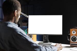 Mens onderzoekt wit Scherm Aan werkstation terwijl telewerken en toepassingen leeg scherm Aan monitor. mannetje ondernemer opereert van een afstand van huis met blanco Chroma sleutel lay-out Aan zijn bureau. foto